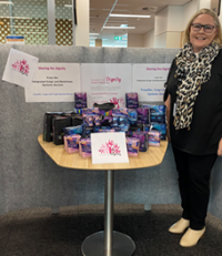 a blonde woman stands in front of a table containing menstrual products