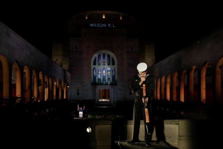 A man dressed in a Royal Australian Navy winter ceremonial uniform plays the didgeridoo at the Australian War Memorial’s Commemorative Area. No one else is around