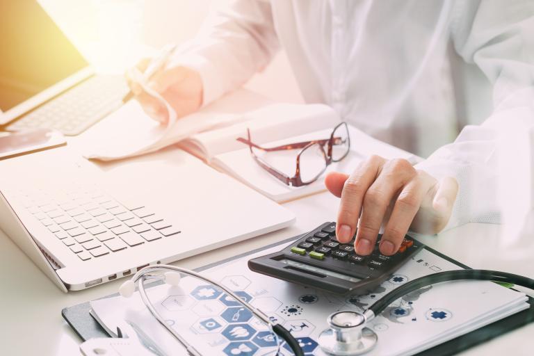 A person sitting at a desk with a computer, calculator, stethoscope and portfolio.