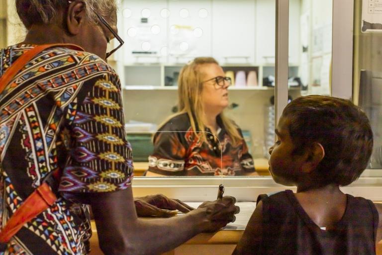 A photograph of a young child and older female First Nations woman completing forms at a service desk.