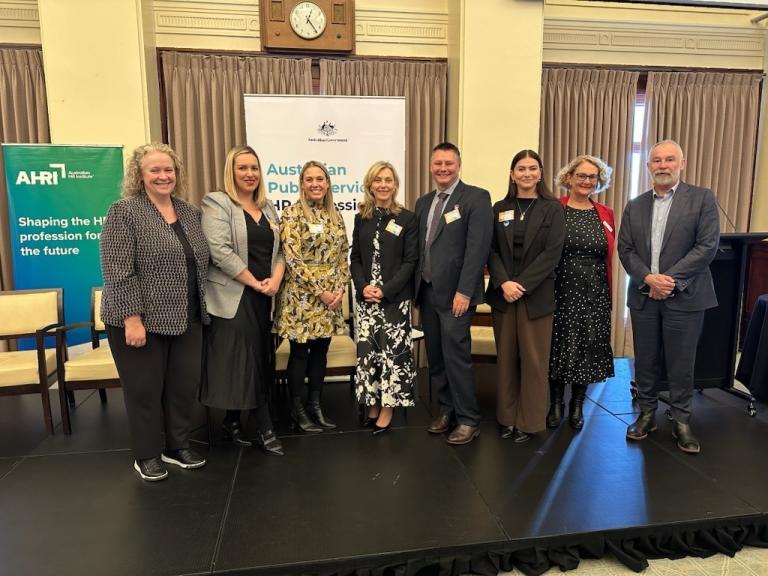 Eight people standing in a row at a networking event in front of pull up banners.