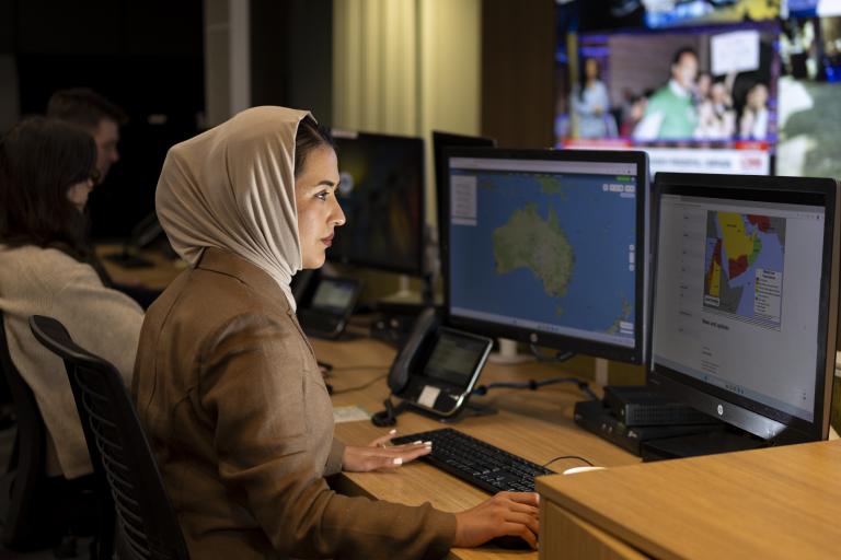 A photograph of DFAT officer Kameleh Safi looking at maps on computer screens as part of her work assisting Australians to depart a conflict zone.