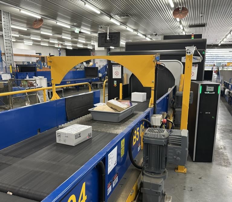 A photograph of parcels on a conveyer belt entering a scanner at the Australia Post Melbourne Gateway Facility.