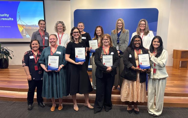 Alternative text: a group of 12 people standing on and in front of a small platform, holding certificates and smiling at the photographer.