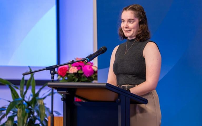 a person standing at a lectern on stage speaking into a microphone
