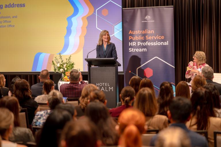 APS HR Head of Profession Jacqui Curtis stands at a podium in front of a HR Professional Stream banner