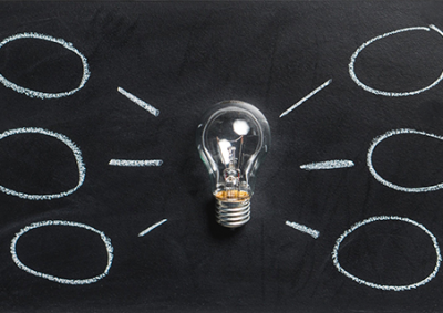 lightbulb resting on a blackboard with idea bubbles sketched around it in chalk.