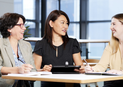 Three female presenting humans sit around a table, talking