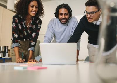 A group of three people crowded around a laptop on a table