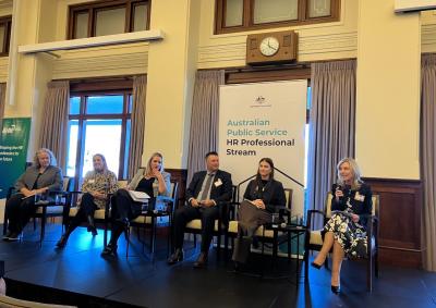 Six people sitting on a panel with microphones, in front of a banner that says Australian Public Service HR Professional Stream.