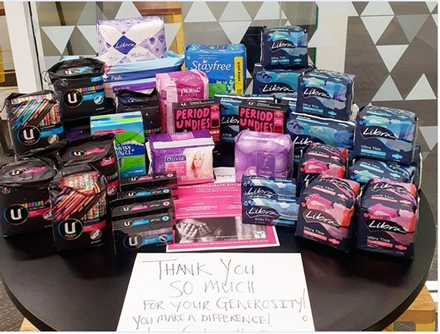 a collection of pads and tampons piled on a table next to a sign reading: thank you so much for your generosity